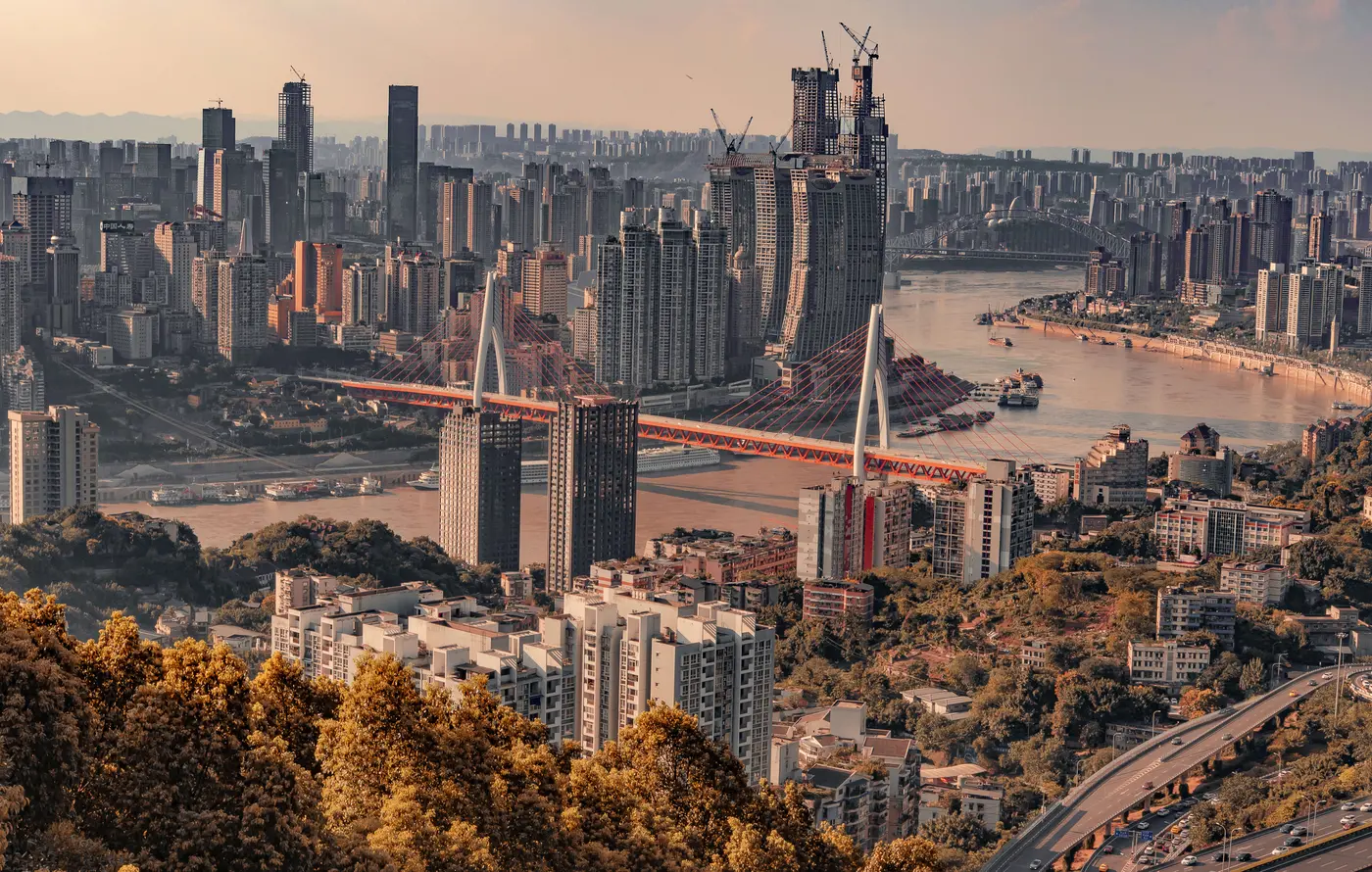 Cakrawala Chongqing dan Sungai Yangtze dalam cahaya musim gugur yang hangat, dengan dedaunan keemasan di latar depan