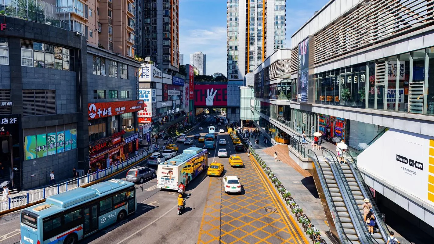 Jalan perbelanjaan Chongqing yang ramai di bawah terik matahari tengah hari musim panas, dengan bus dan taksi lalu-lalang