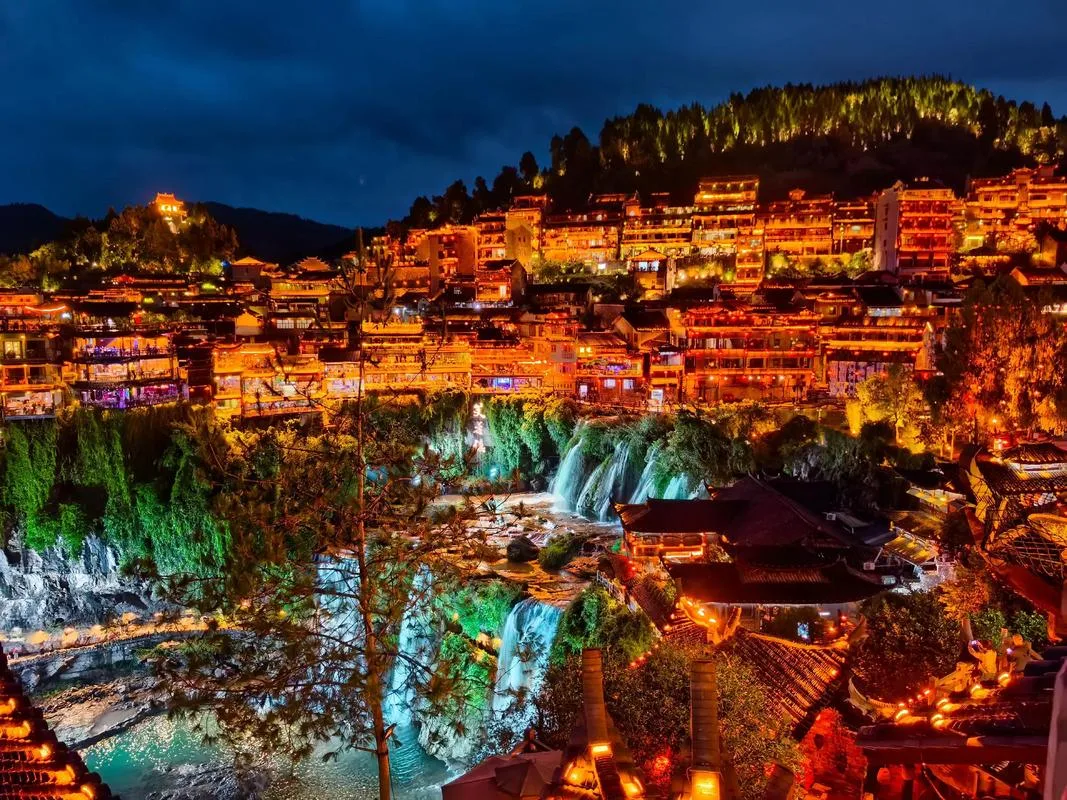 Air terjun dan rumah panggung Furong Ancient Town bermandikan cahaya di malam hari