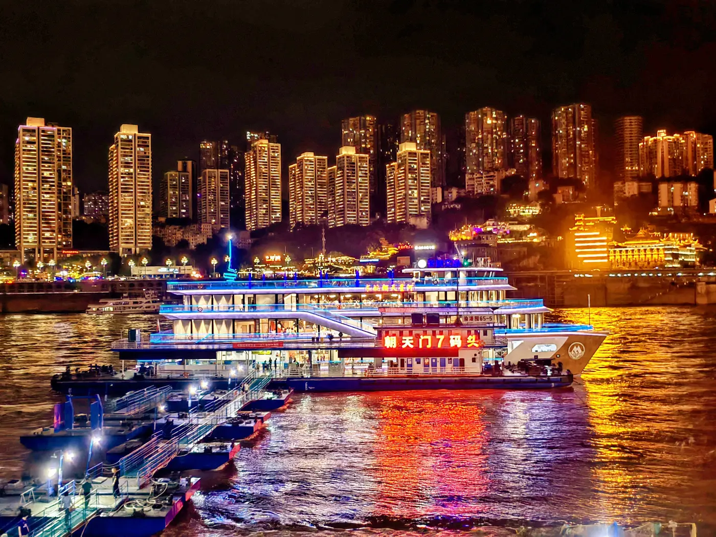 Kapal pelayaran malam Two Rivers di dermaga Chaotianmen dengan skyline Chongqing di belakangnya