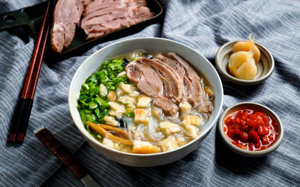 Semangkuk yangrou paomo berisi daging kambing, robekan roti pipih, dan soun, hidangan halal khas Xi'an