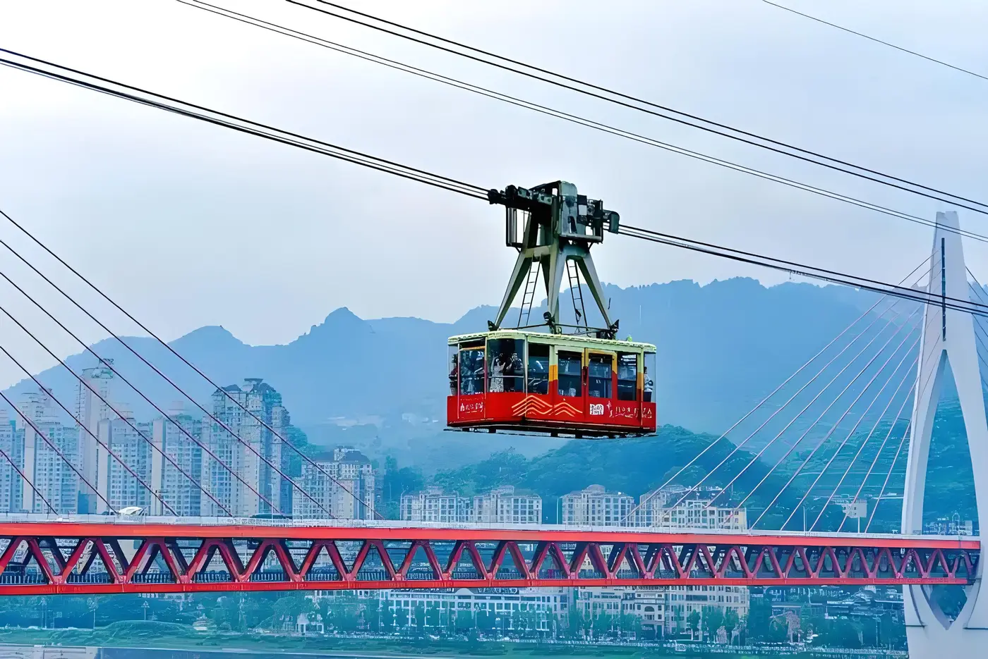 Kabin merah Kereta Gantung Sungai Yangtze menyeberangi sungai dengan Jembatan Dongshuimen di belakangnya, Chongqing