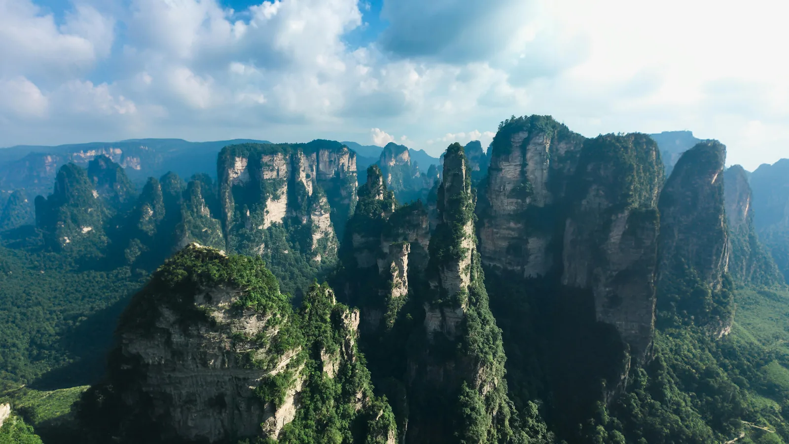 Pemandangan pegunungan dengan puncak berhutan yang dramatis untuk rute Zhangjiajie yang lebih luas