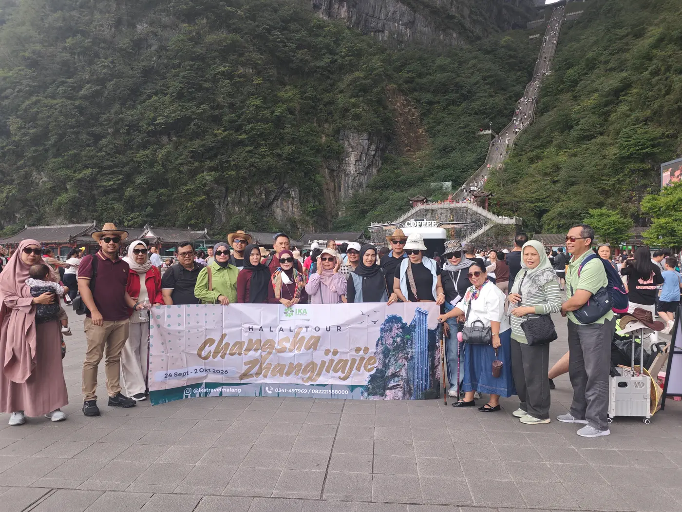 Rombongan tour Muslim berfoto dengan spanduk halal tour di kaki Gunung Tianmen, Zhangjiajie, dengan tangga 999 anak tangga di belakangnya