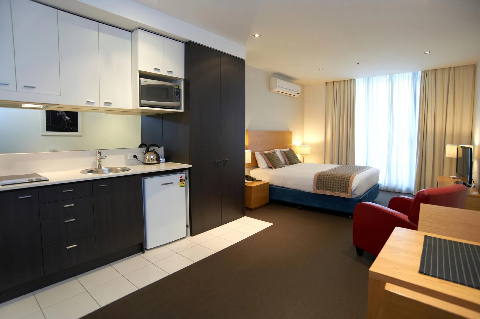 Kamar serviced apartment di China dengan kitchenette berisi microwave, teko listrik, kulkas, dan tempat tidur double dekat jendela